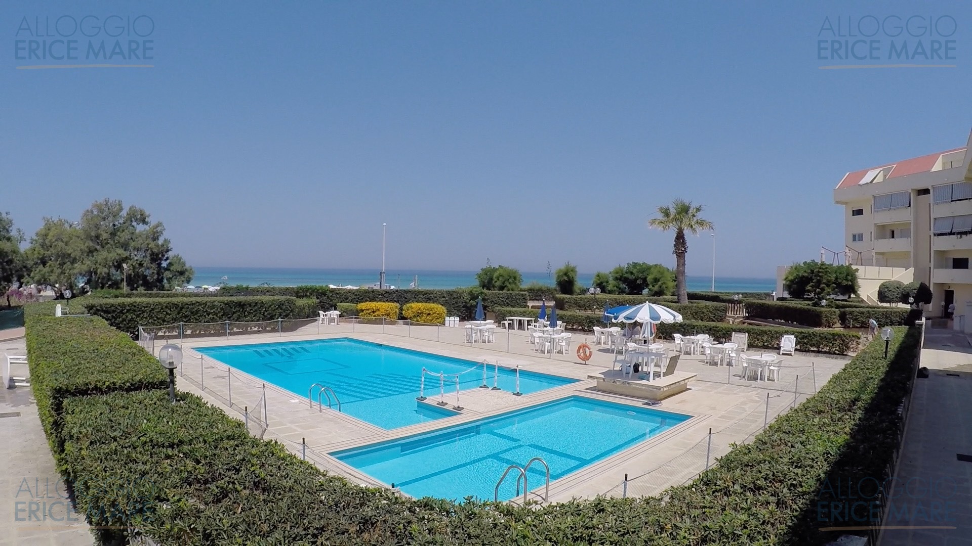 Piscina del Residence Erice Beach vista frontale, con due vasche, area solarium e mare sullo sfondo
